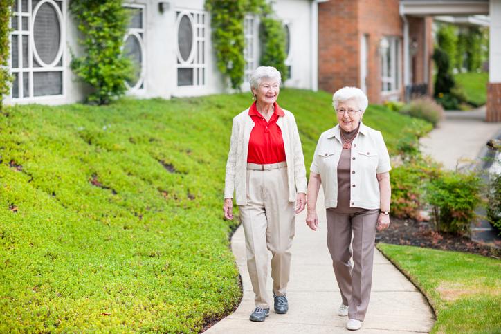 Two senior living community residents take a stroll on well-maintained grounds